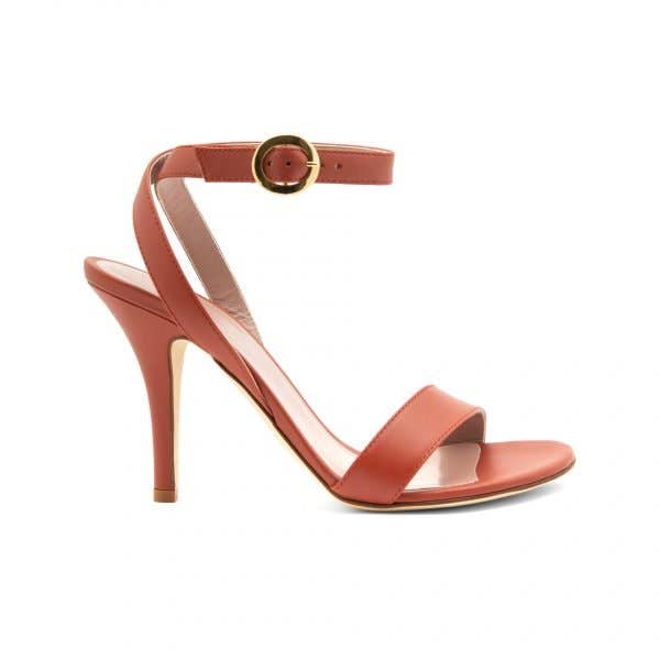A high heeled sandal in a warm reddish-brown color, featuring a single strap over the toes, an ankle strap with a gold buckle, and a slender stiletto heel