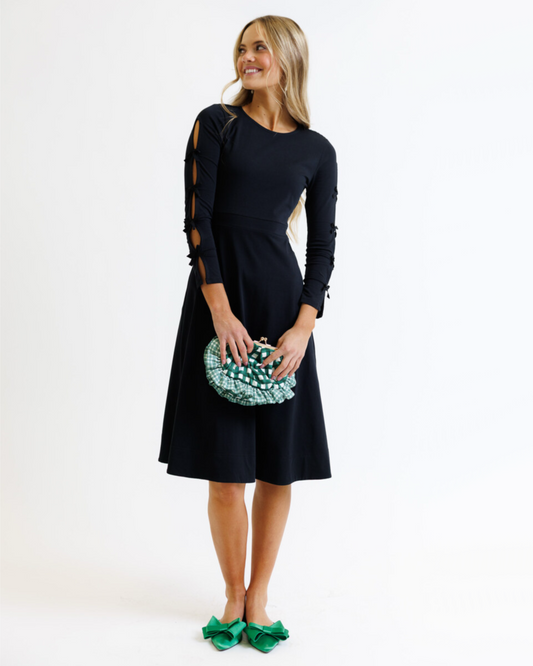 Woman wearing a black dress with cut-out sleeves, holding a green clutch against a white background