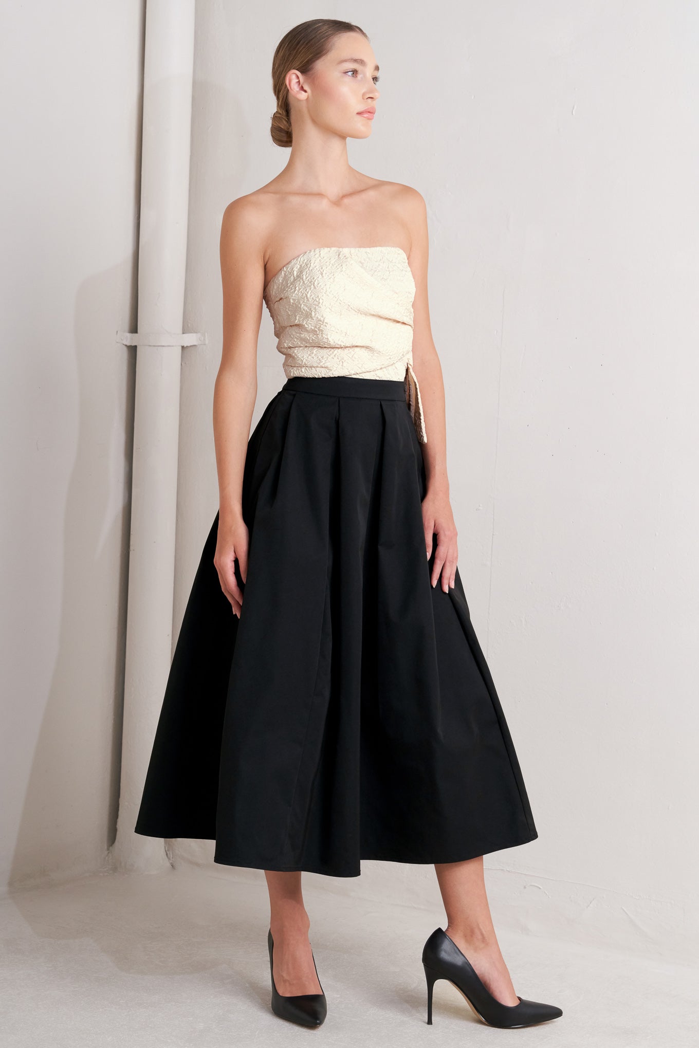 Woman wearing a strapless cream top and black skirt against a plain background