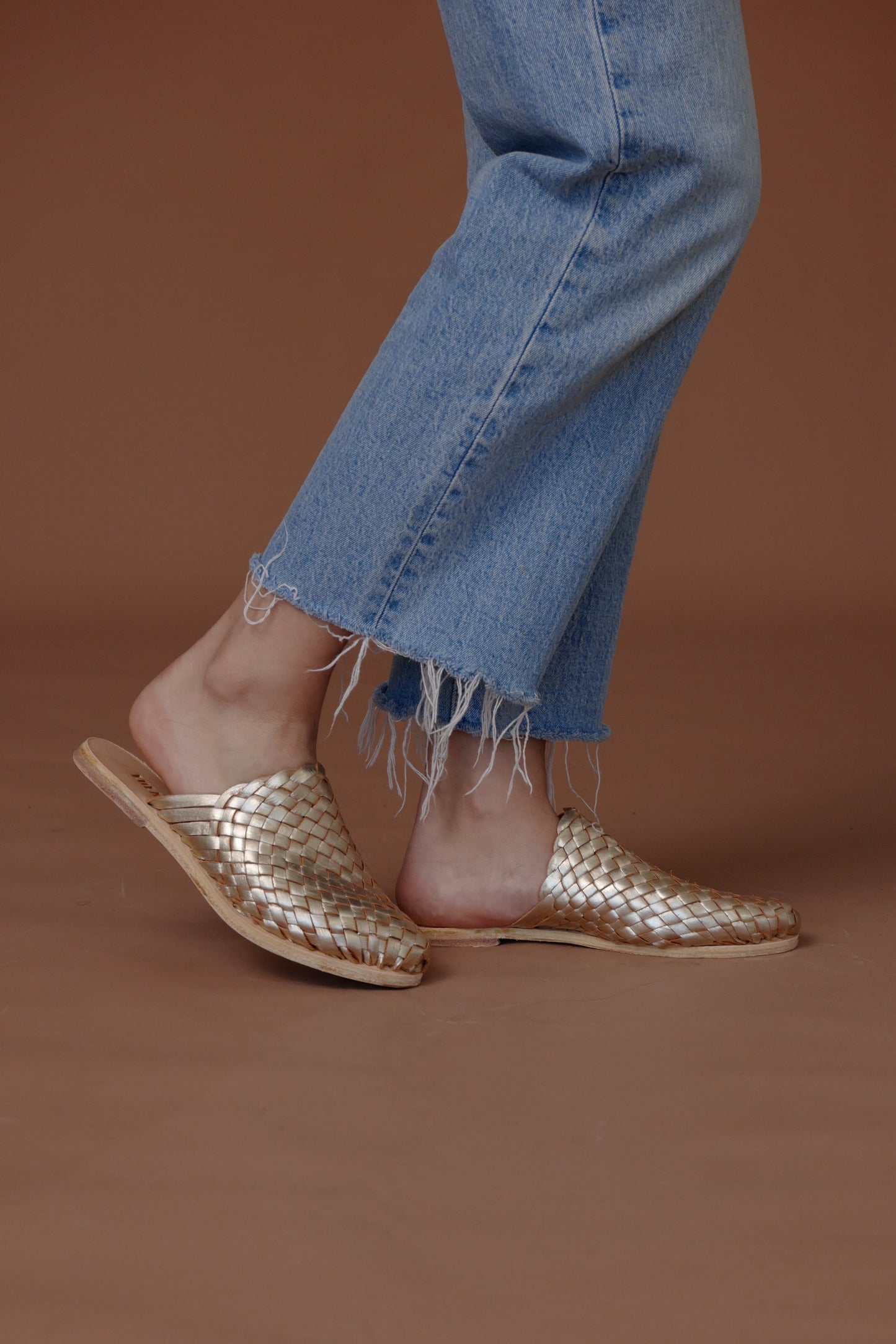Gold woven sandals worn with blue jeans on a brown background