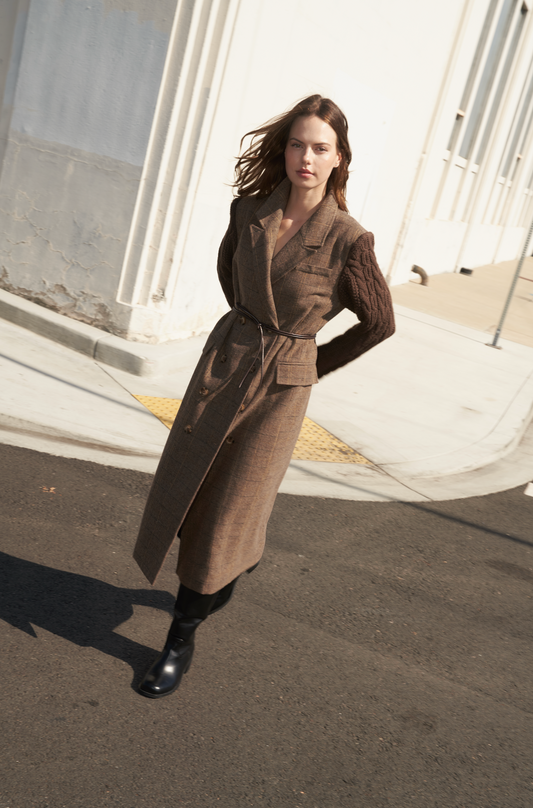 Woman in a brown coat standing on a street with classical architecture in the background